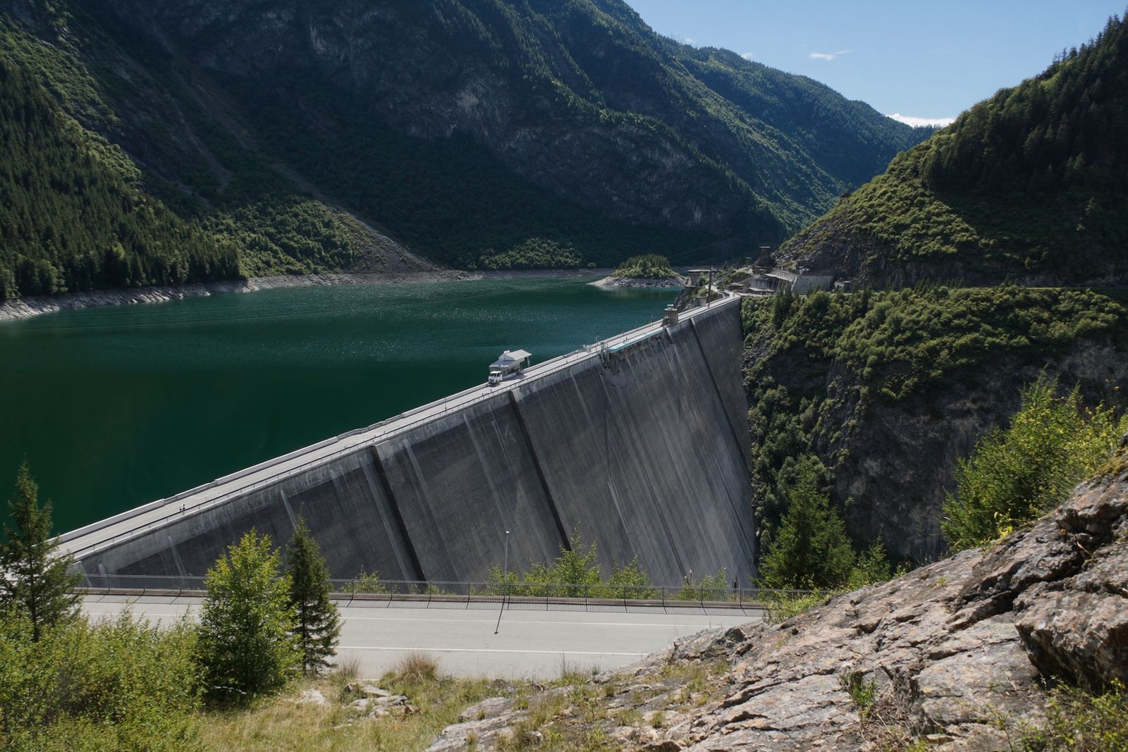 A concrete hydroelectric dam holding back an emerald reservoir in a wooded mountain gorge
