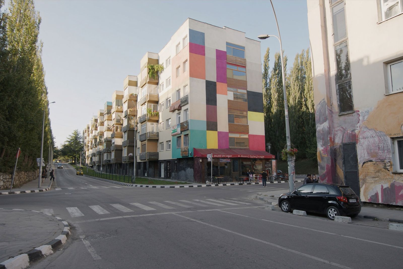 An apartment block with a facade painted in bright colour patches on a sunlit city street