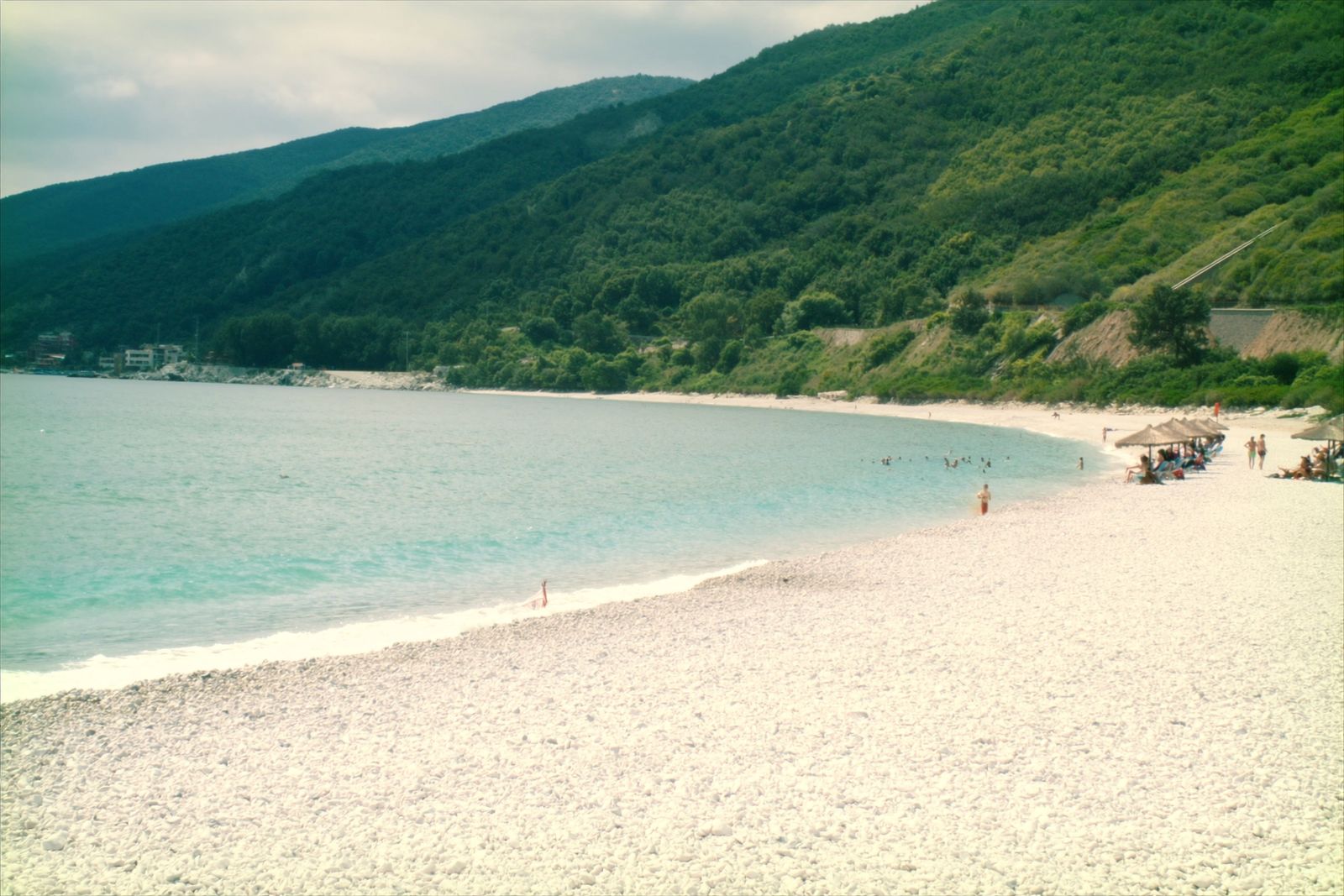 A long white pebble beach with straw umbrellas and clear turquoise water in high summer